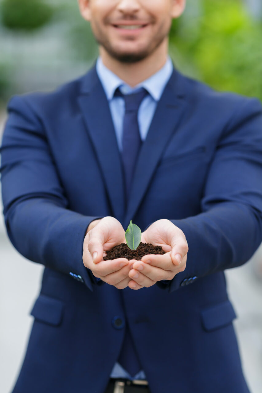 Close up of businessman holding dirt and leaf in his hands